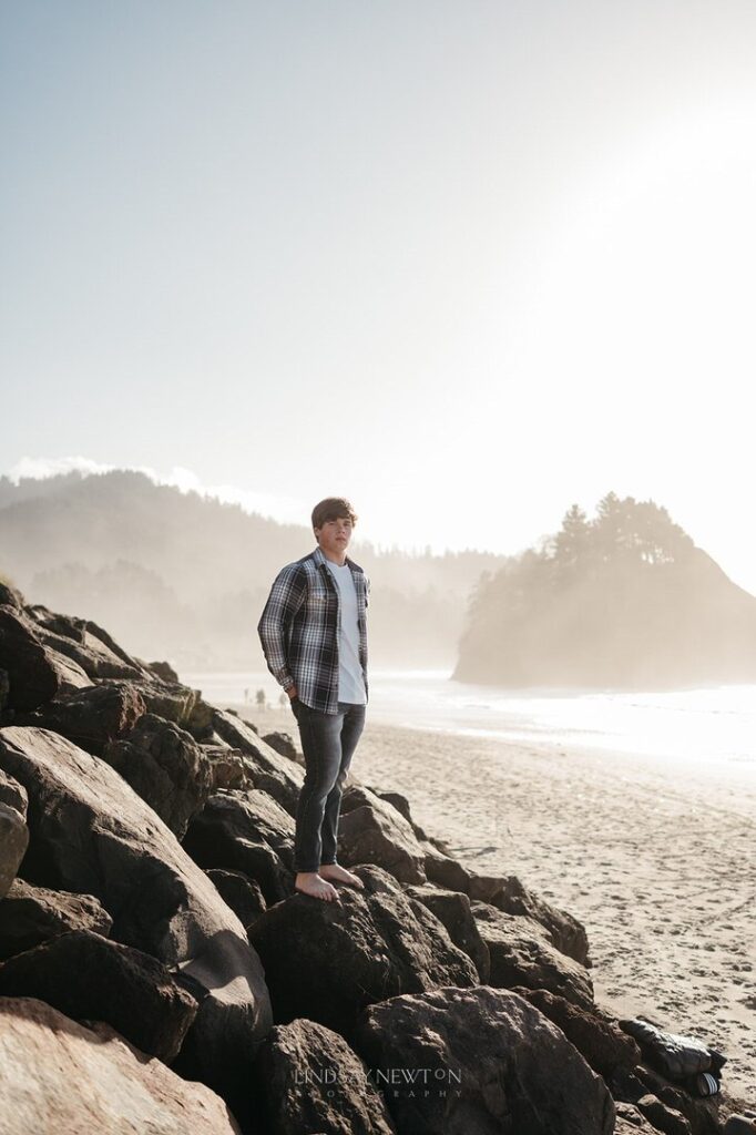 Guy standing on some rocks next to the water with mountains in the background